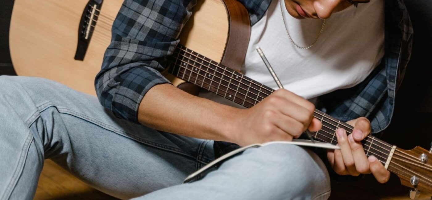 Musiker schreibt beim Spielen einer Akustikgitarre Notizen auf